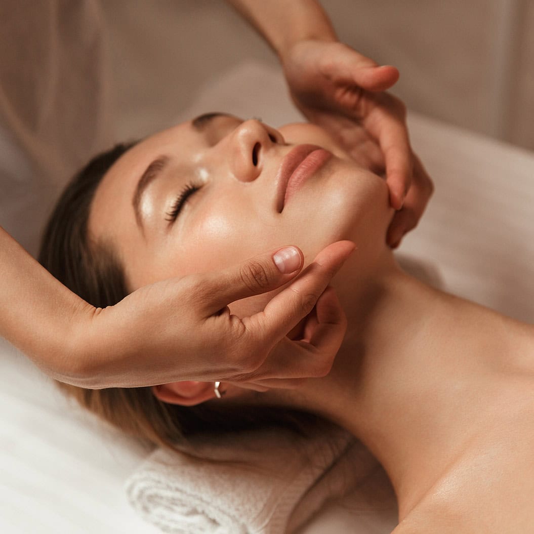Person bei entspannender Gesichtsmassage, geschlossene Augen, friedlicher Ausdruck, warme Hauttöne.