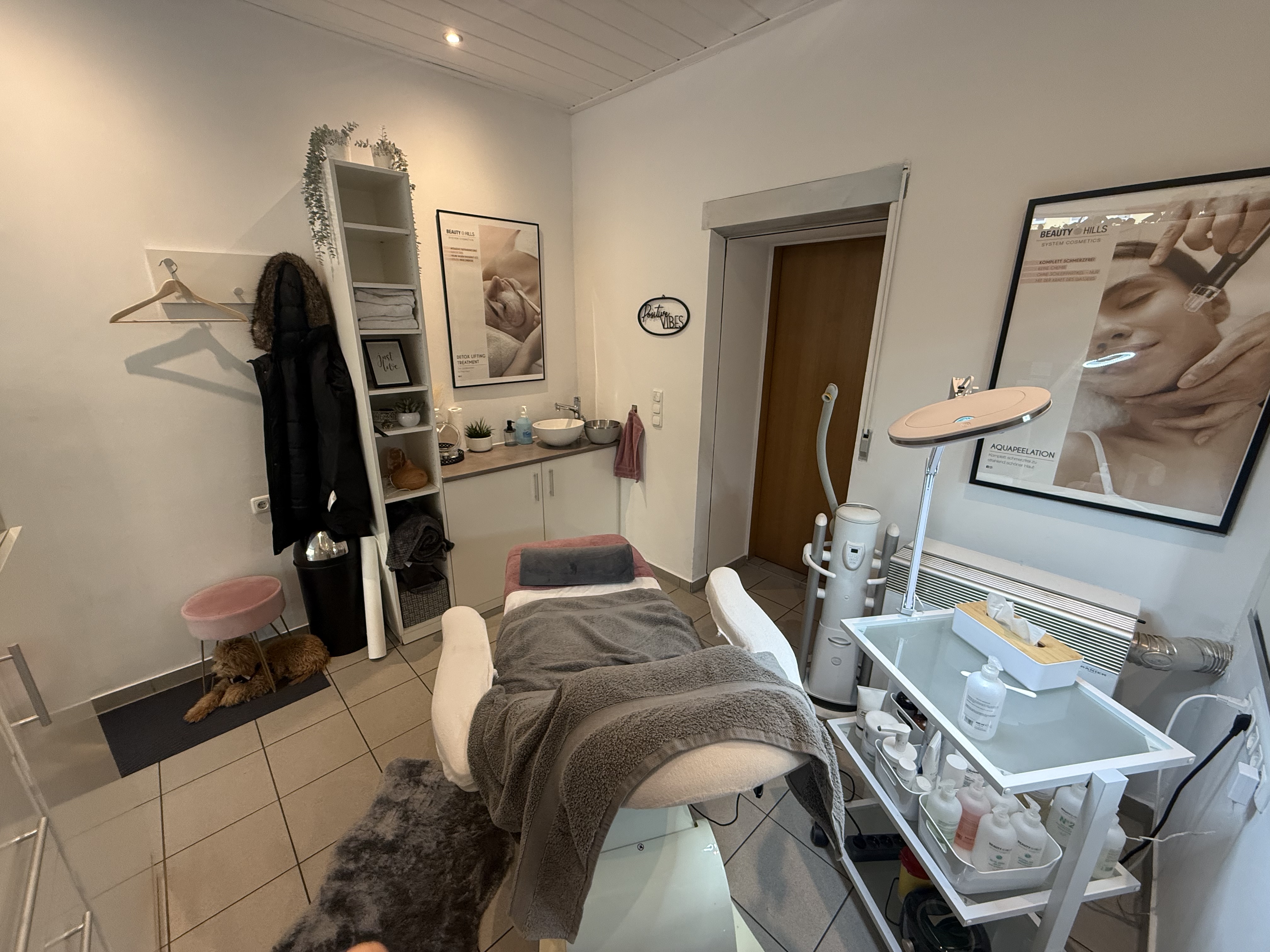 Helles Behandlungszimmer mit Kosmetikliege, Pflegeprodukten und dekorativen Postern